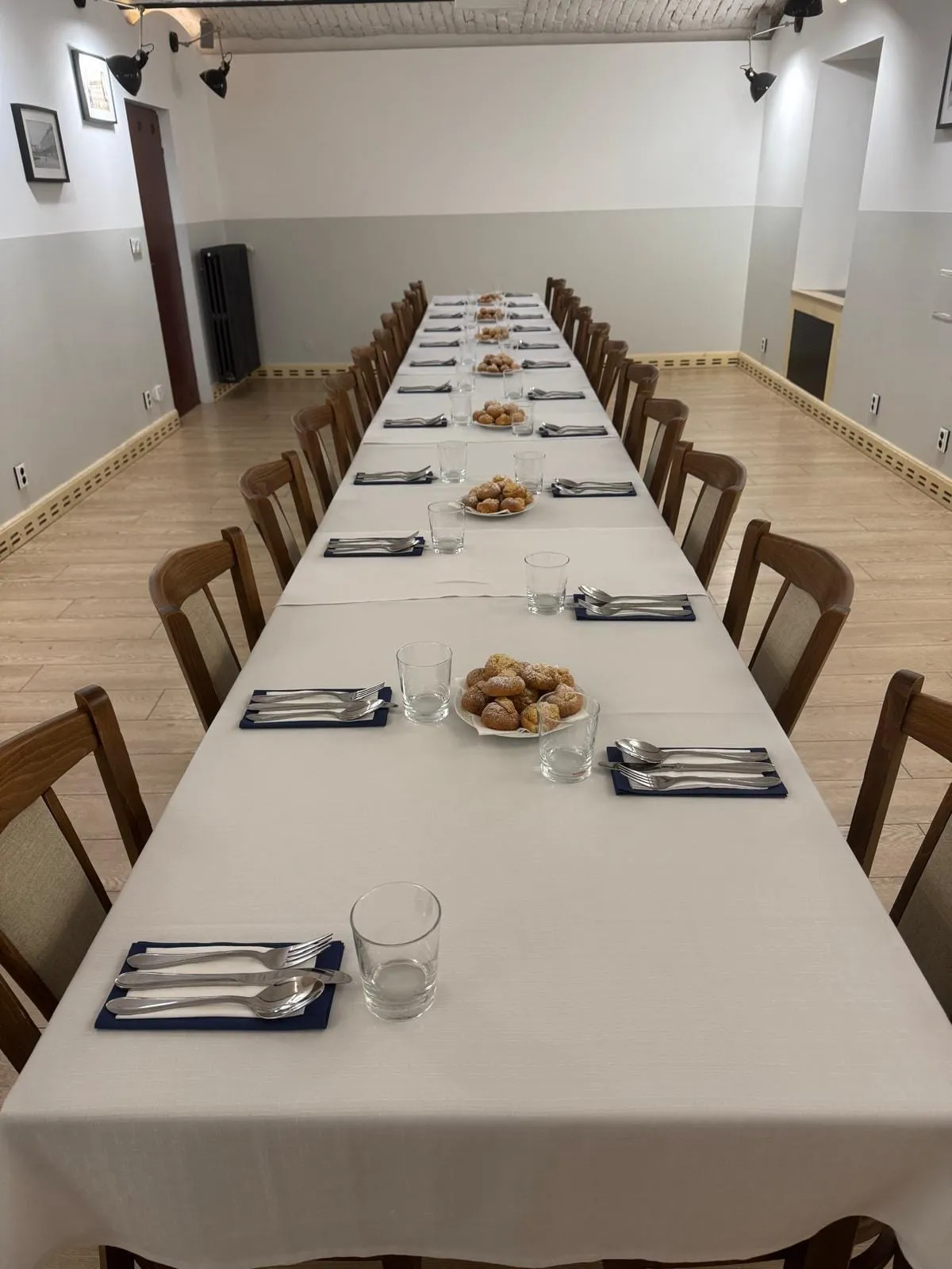 Sál s dlouhou prostřenou tabulí pod klenutým stropem, coffee break s koblihami